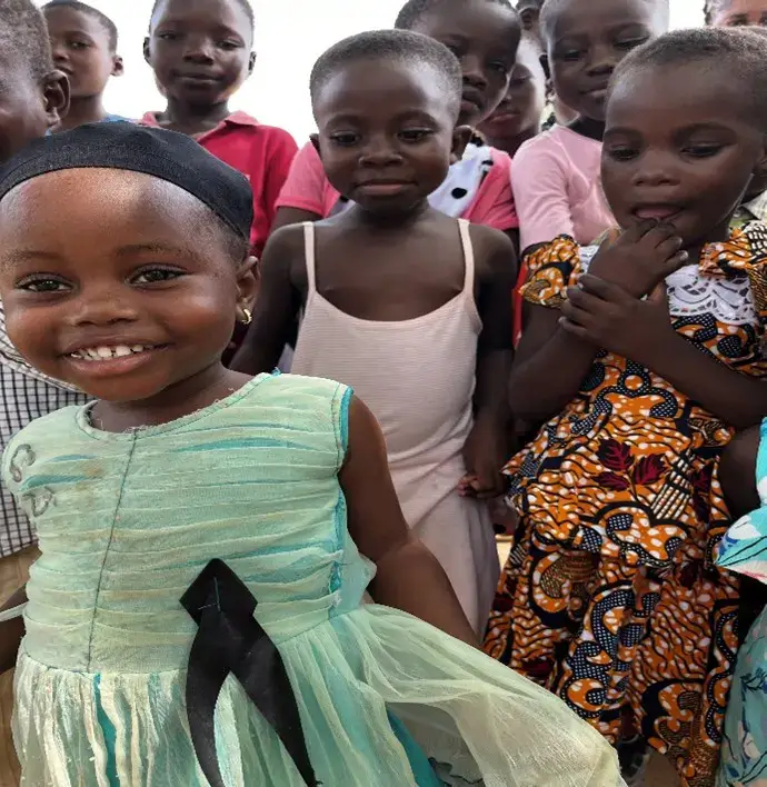A close-up of a smiling young girl in a light blue dress with other children in colorful attire