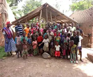 A large group of children and adults posing together outside a rustic structure